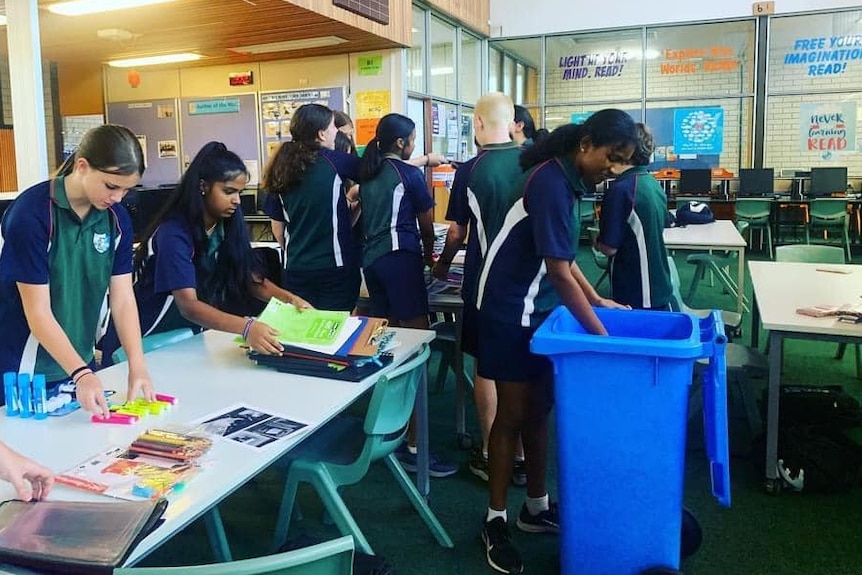 A group of school students in blue and green uniforms at a table sorting stationery supplies.