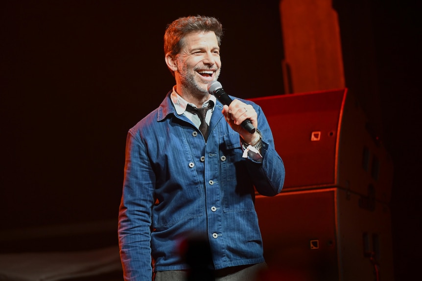 Zack Snyder standing on a stage in a blue jacket holding a microphone