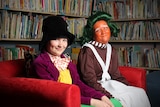 Children dressed as Willy Wonka and an oompa loompa sit on a couch in front of a book case.