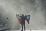 An anti-government protester stands in a cloud of tear gas holding up the red white and blue Chilean flag