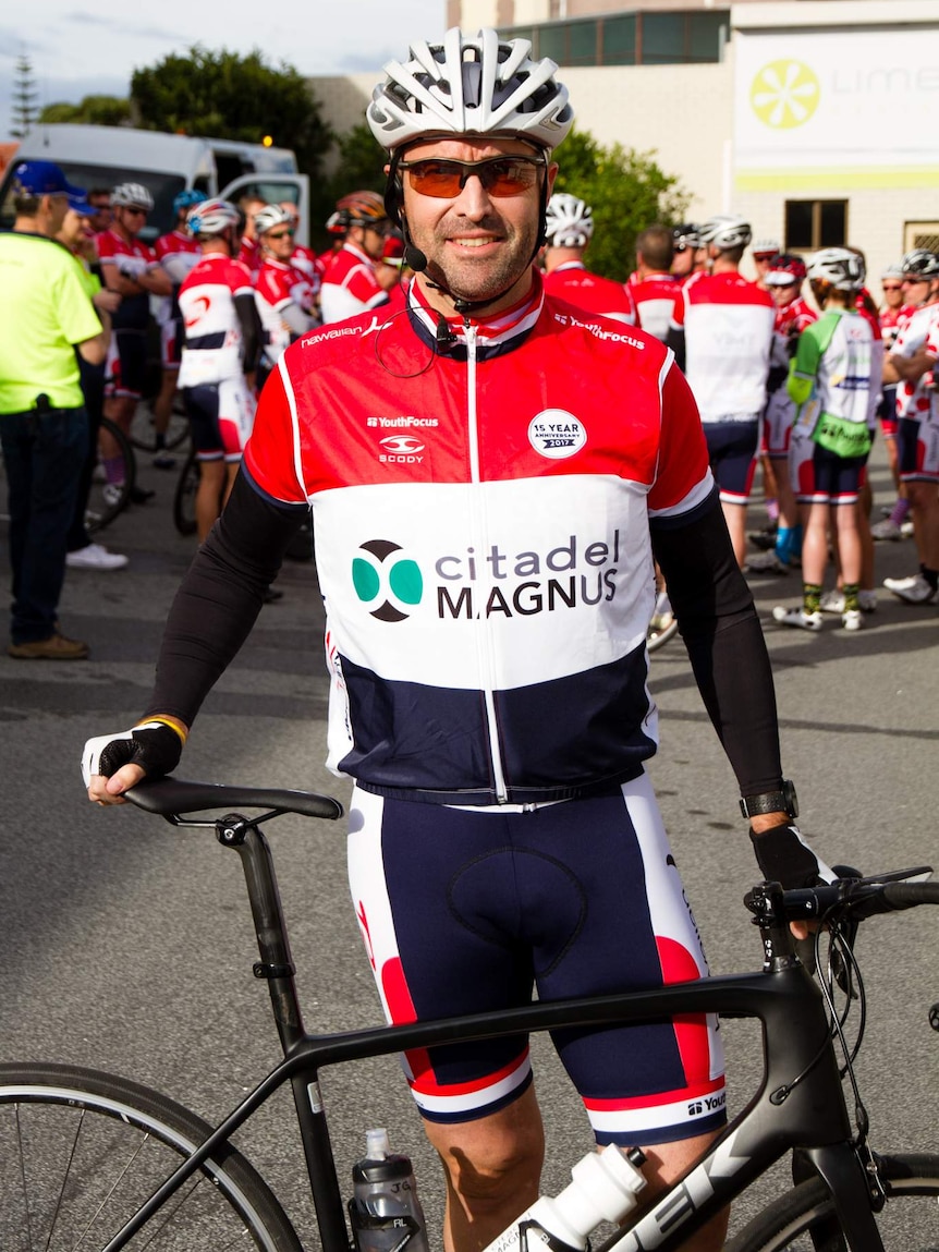 A profile pic of a man in cycling gear standing next to a bike.