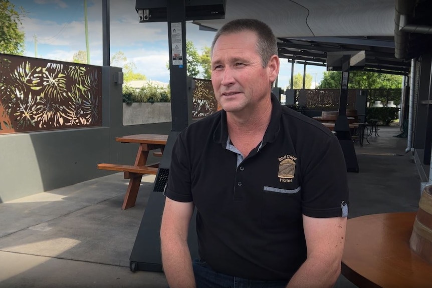 Un homme en chemise noire est assis à côté d'une table de tonneau dans un café en plein air en béton.