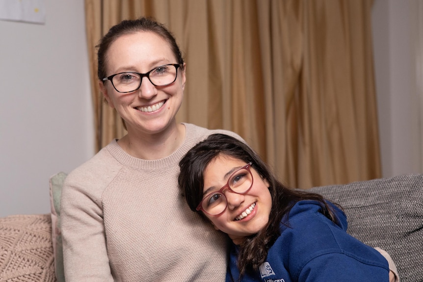 A woman wearing glasses and her daughter wearing glasses and a blue top smile for the camera