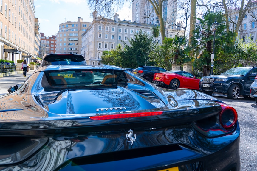 A Ferrari parked on a London street, near several other sports cars and a BMW 