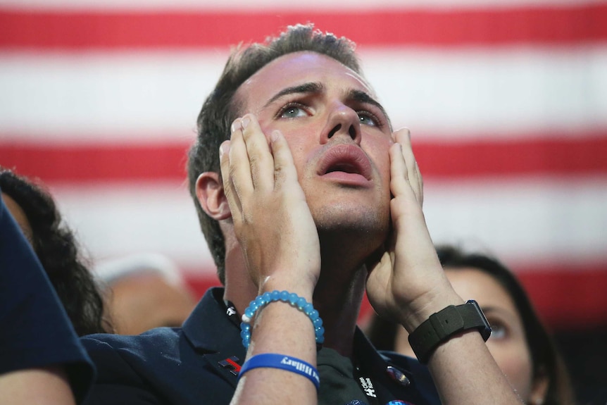 An anxious Hillary Clinton supporter holds his hands to his face.