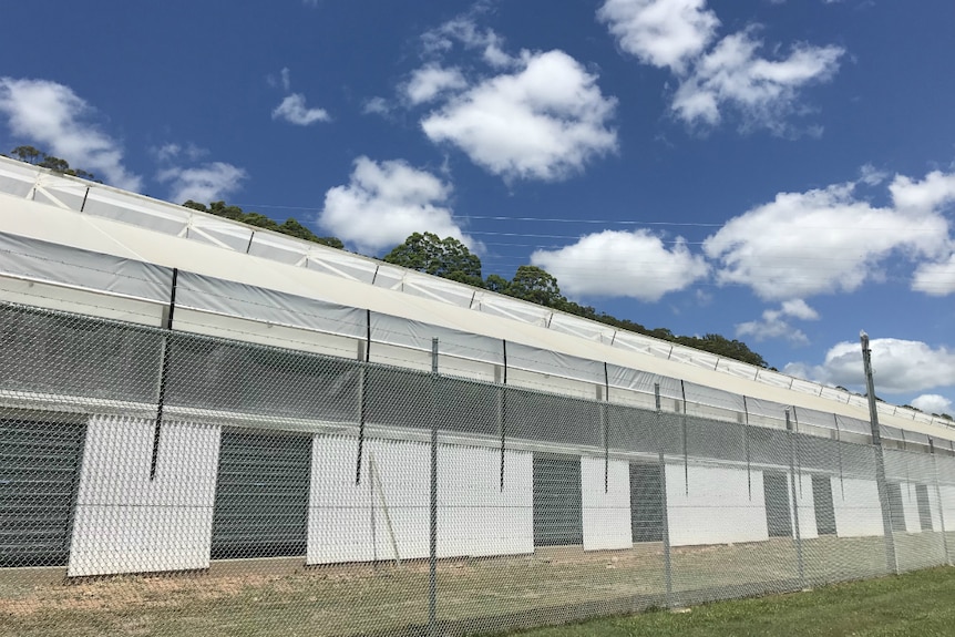 Big white building behind a high fence topped with barbed wire.