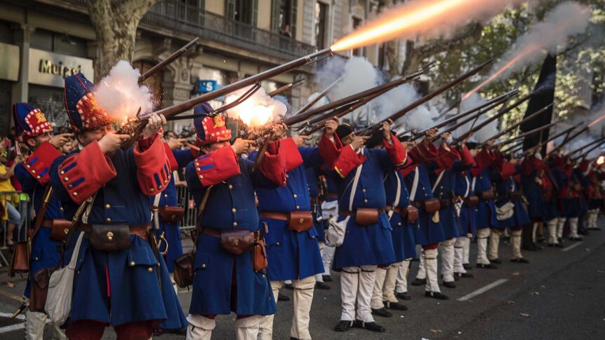 Men wearing reproductions of Catalan military costumes shoot weapons during a display.