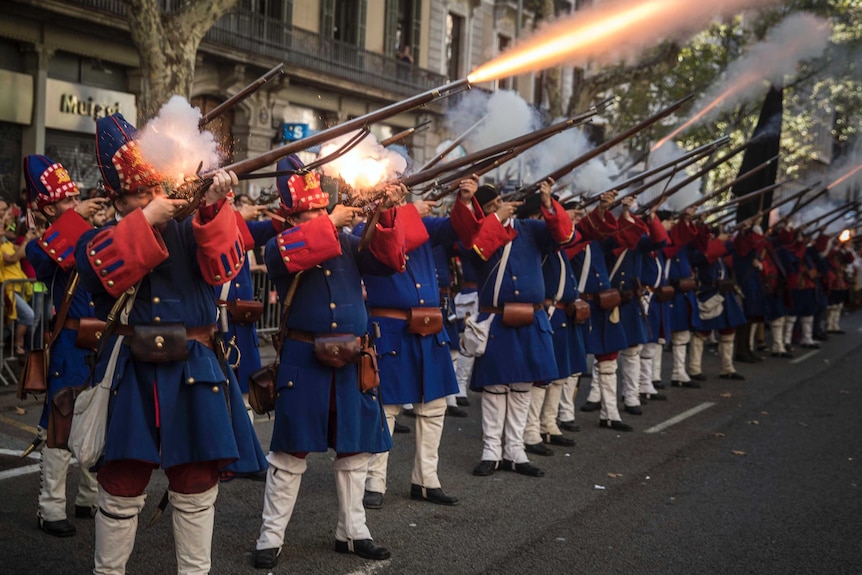 Men wearing reproductions of Catalan military costumes shoot weapons during a display.