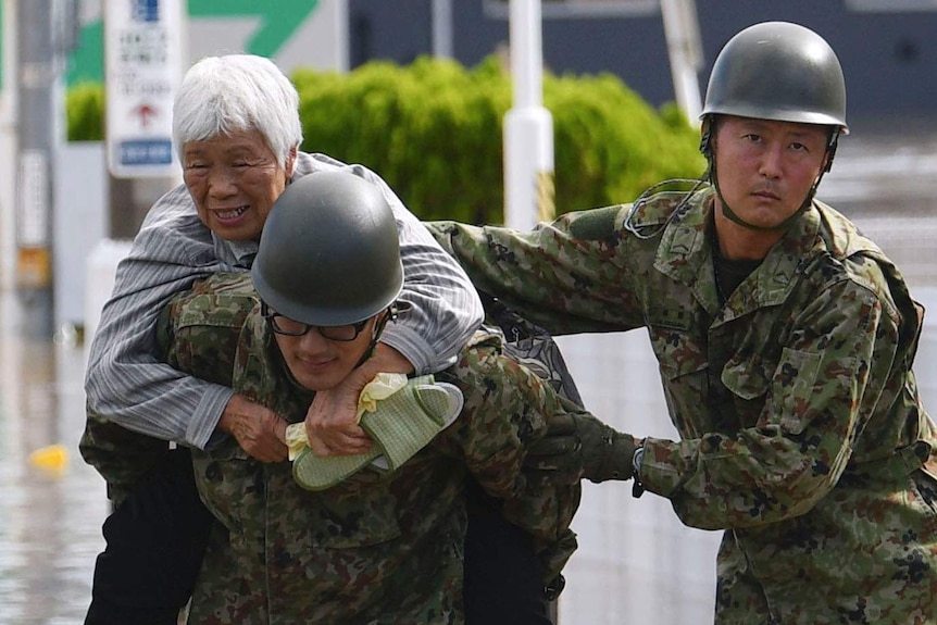 An elderly resident is carried by two members of the Japanese military, during evacuations caused by Typhoon Hagibis.