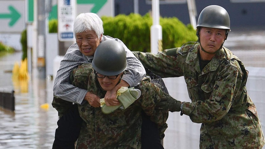 An elderly resident is carried by two members of the Japanese military, during evacuations caused by Typhoon Hagibis.