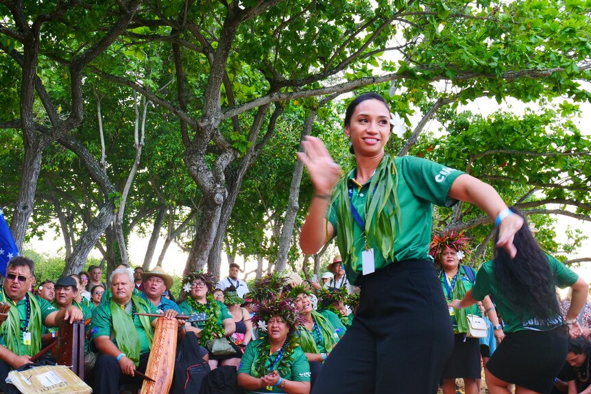 A woman wearing green dances while others look on.