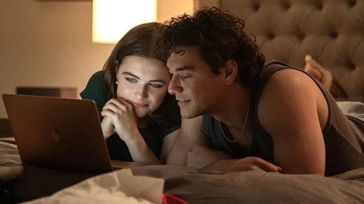 Two people lying in bed watching a laptop.