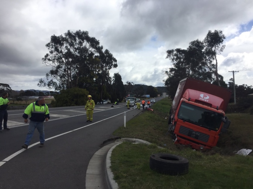 Emergency services workers, wearing hi-vis vests, on stand on a road. A damaged Australia Post van is in the ditch beside it