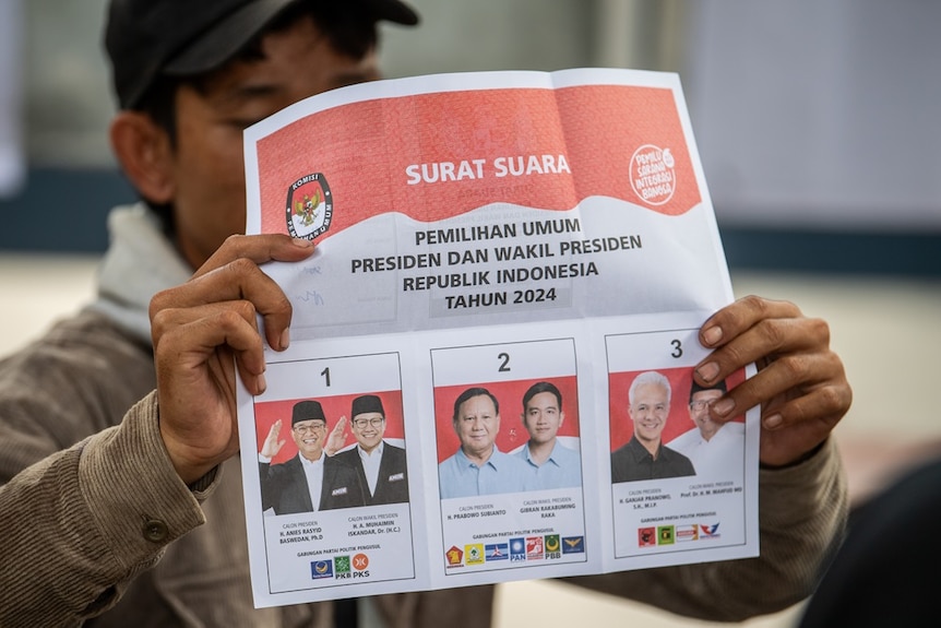 Мужчина держит бюллетень с фотографиями кандидатов в президенты Индонезии.