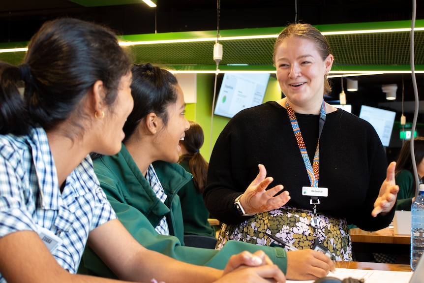 A young woman talks smiling to two female high school students