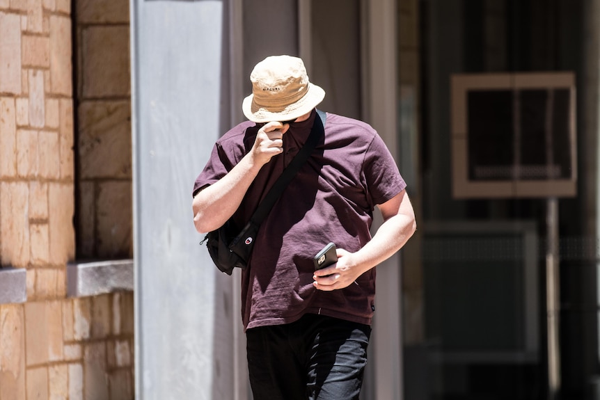 A man pulls his T-shirt up over his face to avoid media outside a courthouse.