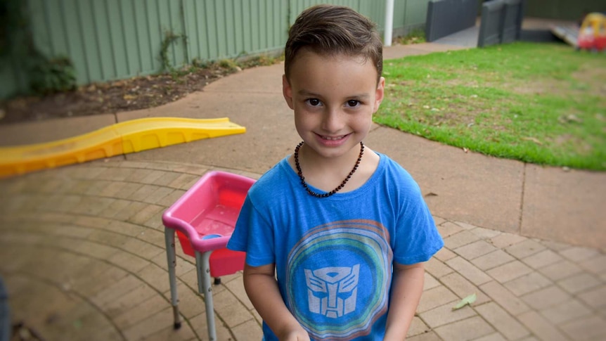 Young boy with smile wearing blue shirt with toys in background