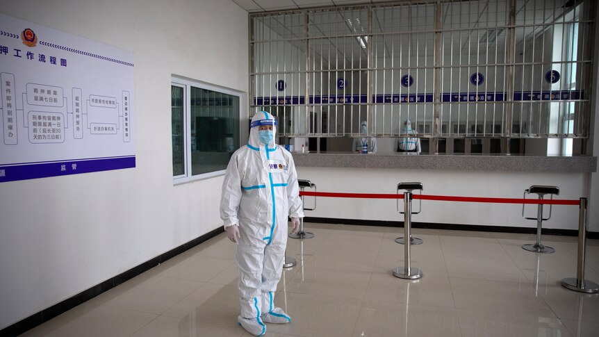 A security officer in a protective suit stands in a reception area at a detention centre. 