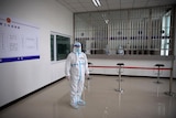 A security officer in a protective suit stands in a reception area at a detention centre. 