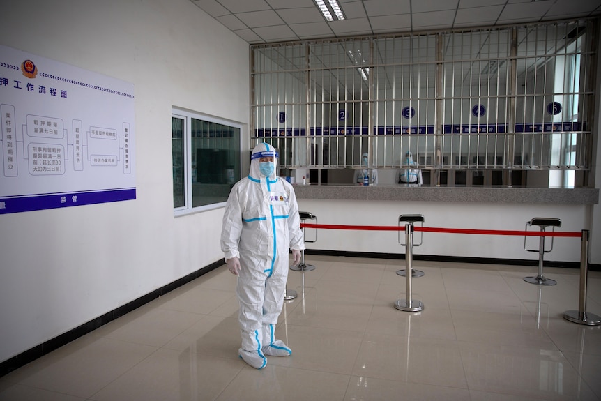 A security officer in a protective suit stands in a reception area at a detention centre. 