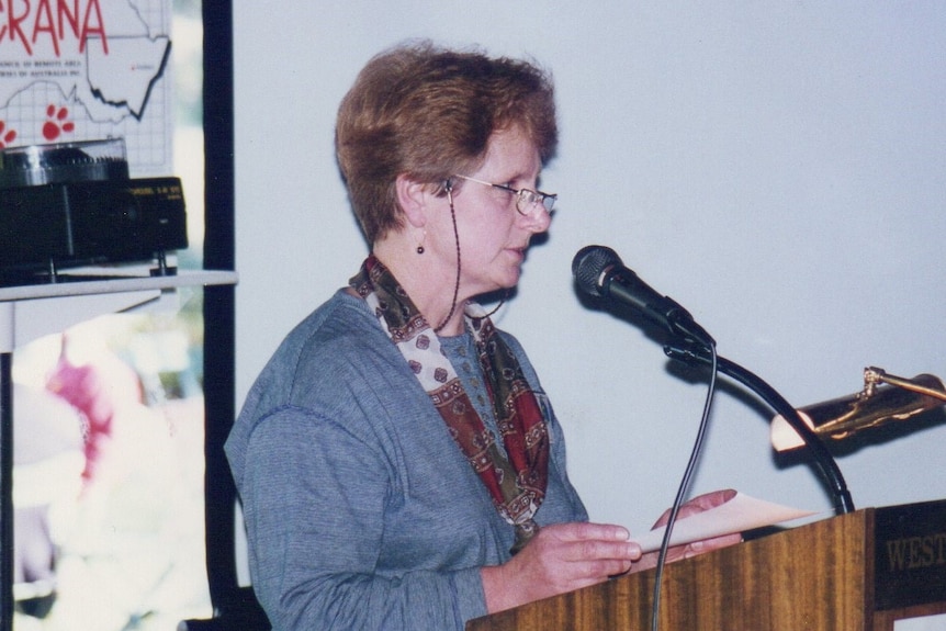a woman in a gray suit jacket at a lectern.