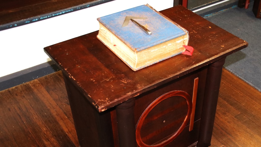 A blue bible with a an arrow on its cover sitting on a wooden desk with other masonic symbols