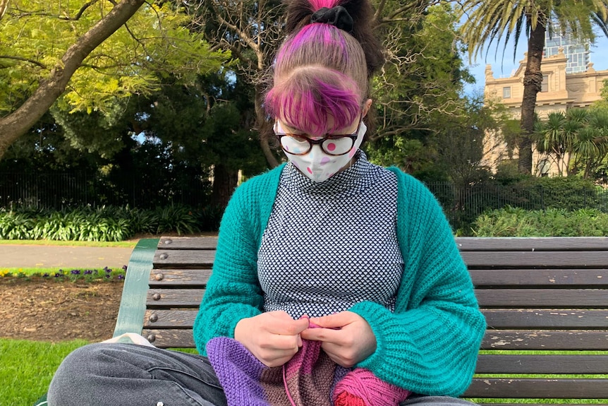 A young woman knitting on a park bench.