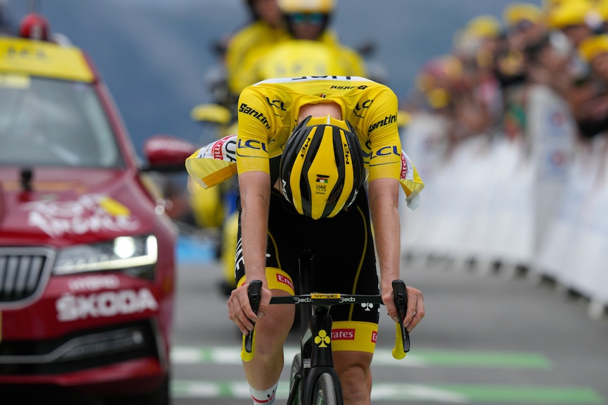 A cyclist wearing the yellow jersey bows his head in disappointment as he crosses the line at the end of a Tour de France stage.
