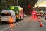 A green bus on the side of a road marked by witch's hats