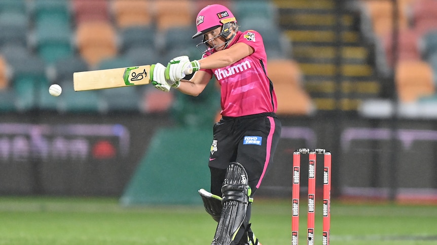 A Sydney Sixers WBBL cricketer stares intently at the ball as she swings at a delivery during a game.