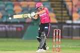 A Sydney Sixers WBBL cricketer stares intently at the ball as she swings at a delivery during a game.
