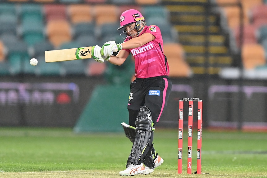 A Sydney Sixers WBBL cricketer stares intensely at the ball as she swings after a delivery during a match.