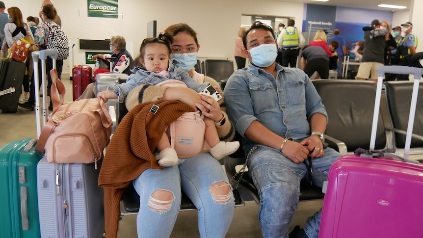 A woman holds and young girl while seated next to a man with three suitcases next to them