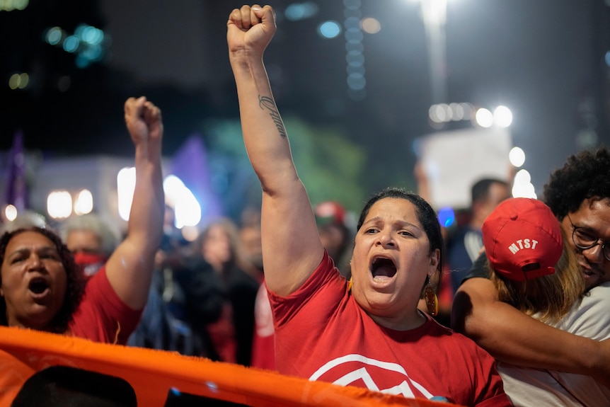 A woman dressed in red raises her arm in the air during an anti-Bolsonaro protest.