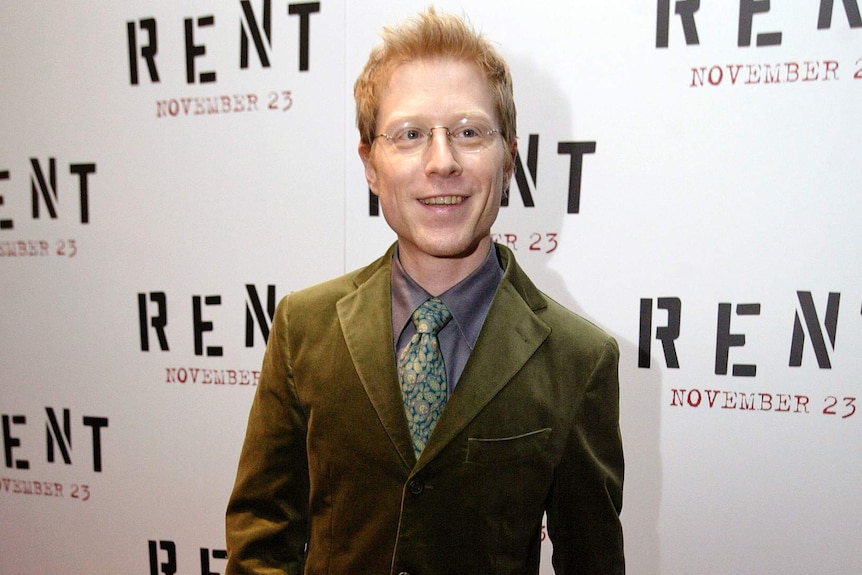 Actor Anthony Rapp wears an olive green suit and stands on the red carpet at the Rent premiere.