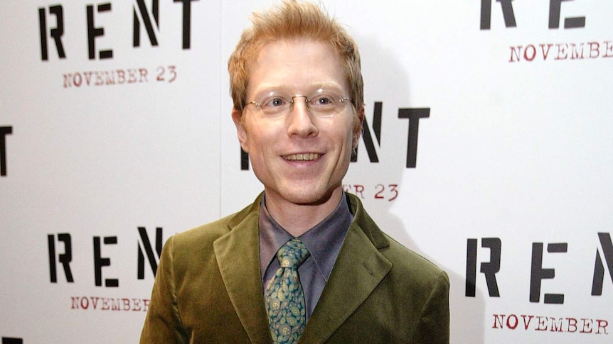 Actor Anthony Rapp wears an olive green suit and stands on the red carpet at the Rent premiere.