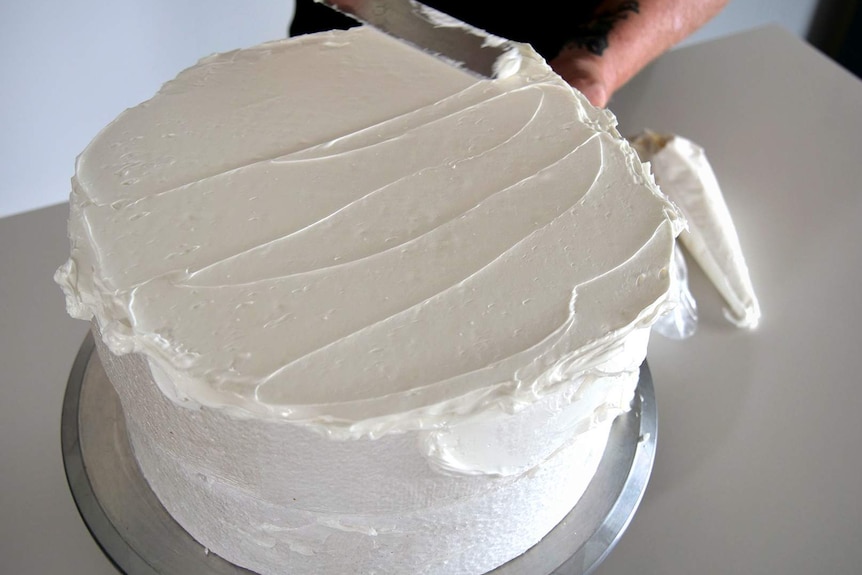 Close up photo of a woman's hands decorating a polystyrene block to look like a cake
