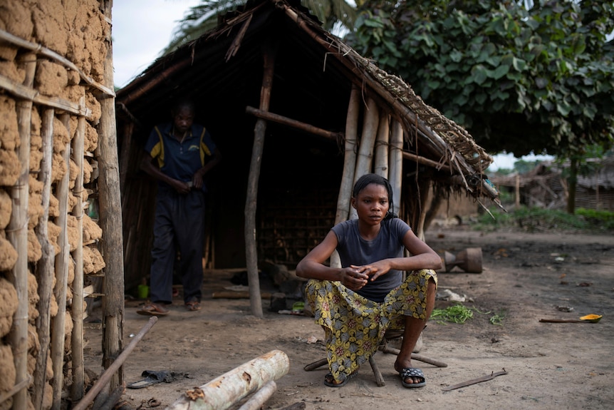 a woman sits in front of a house in Yaboya village