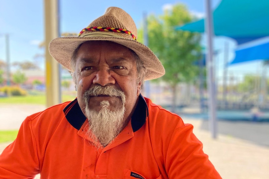 An Indigenous man in a wide brimmed hat and an orange shirt 