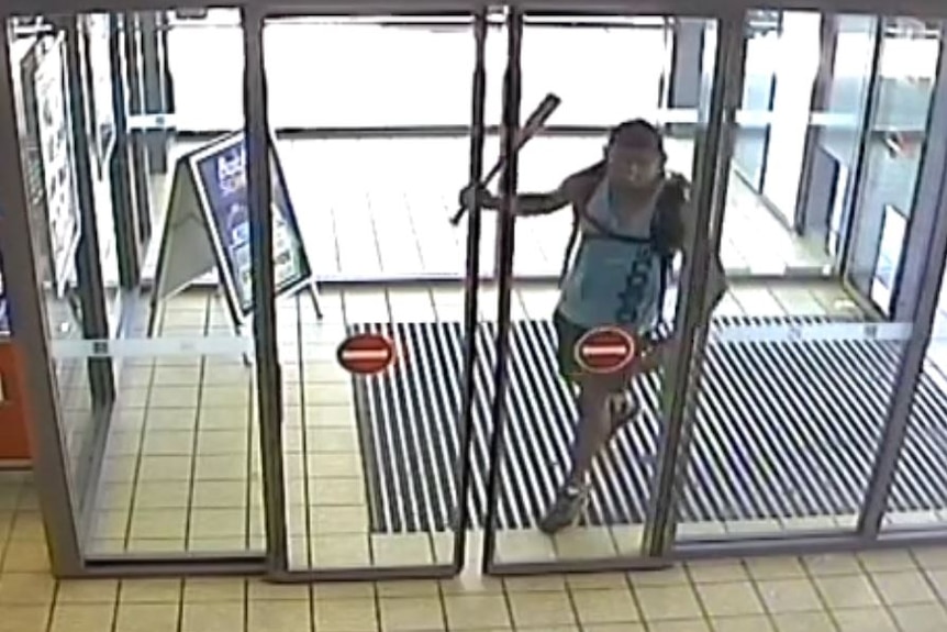 A screenshot from CCTV of a man entering a supermarket holding a baseball bat.
