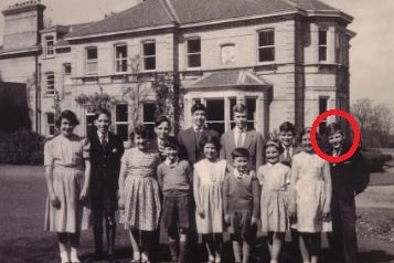 A black and white photo of 13 well dressed smiling children outside a two-storey building.