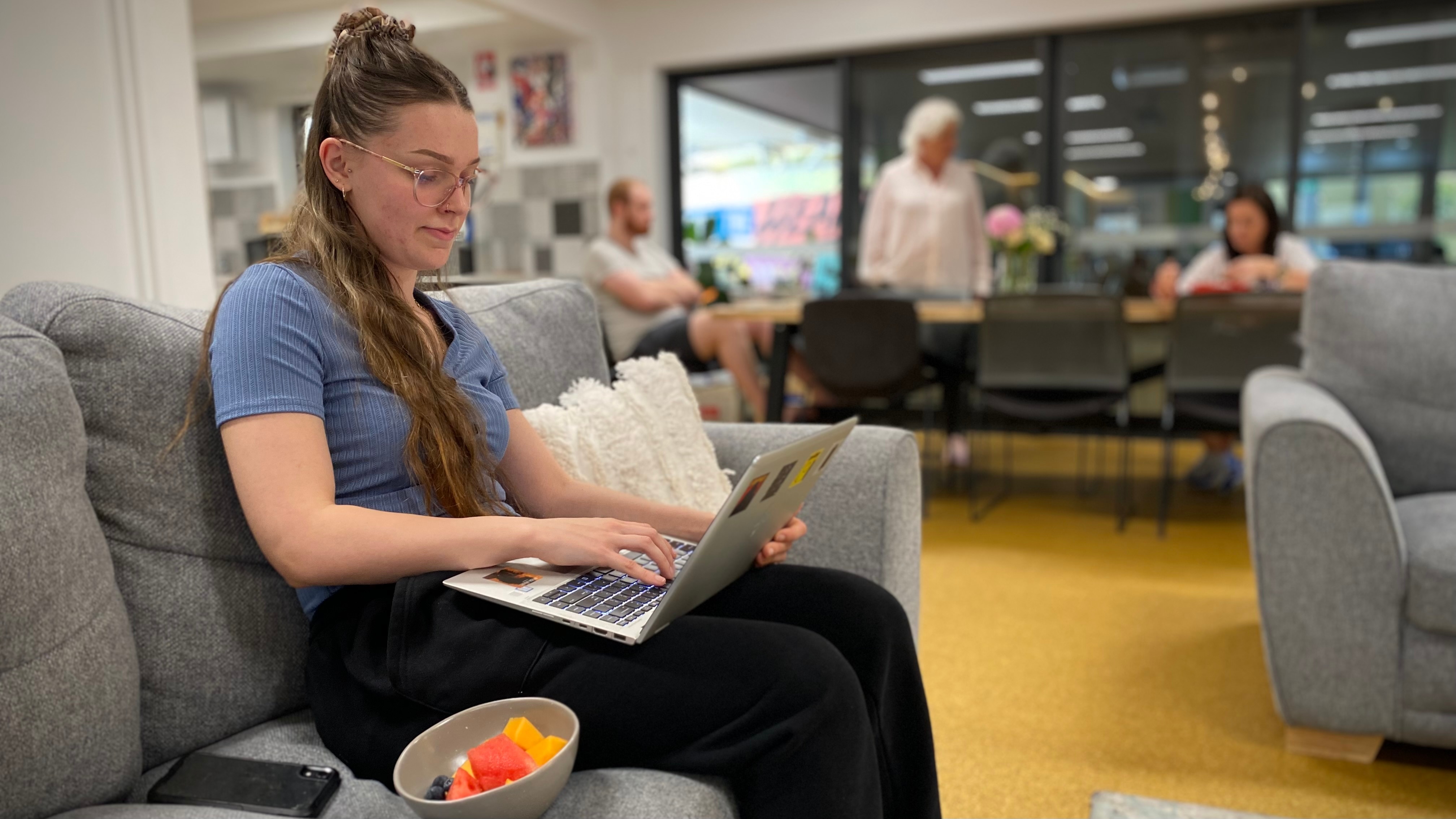 A teenage girl sits on a couch with a laptop.