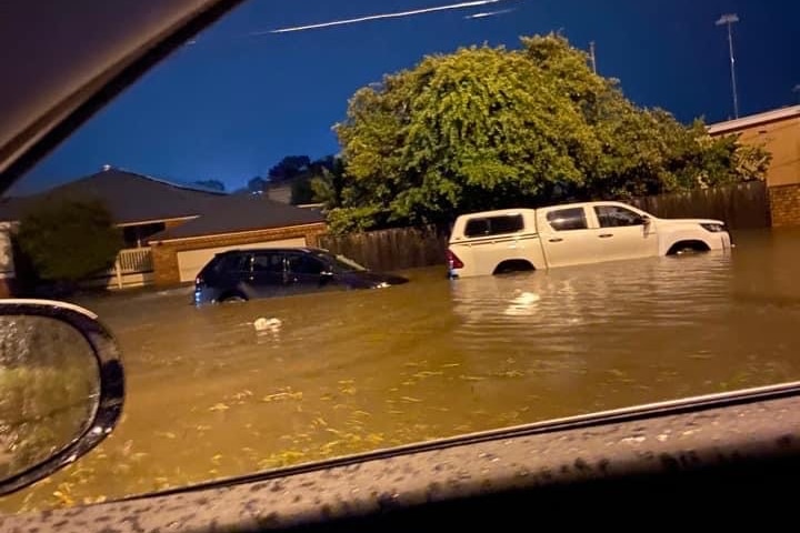Flash flooding on a suburban road, up to the wheels of a tall car.