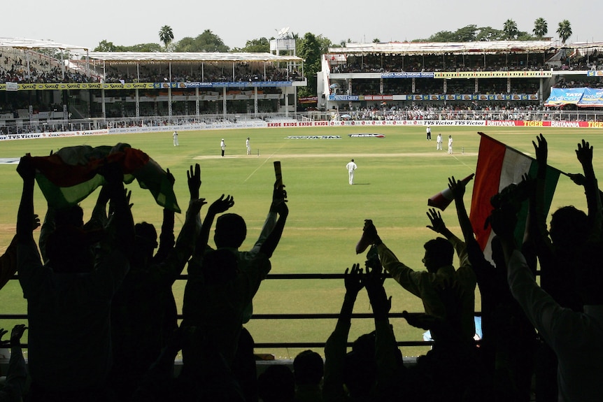 Fans cheer while looking out at the cricket pitch as seen from behind