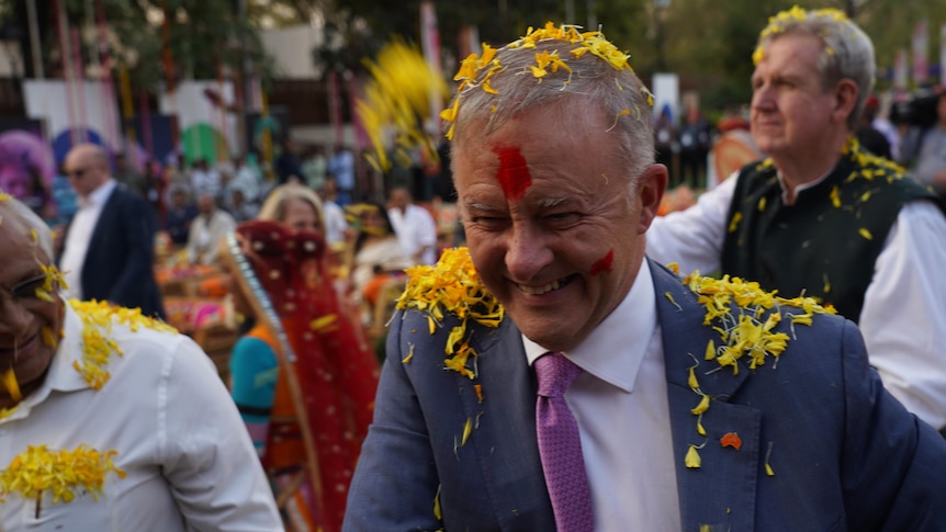 Anthony Albanese smiling as yellow flower rain down during Holi event.