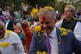 Anthony Albanese smiling as yellow flower rain down during Holi event.