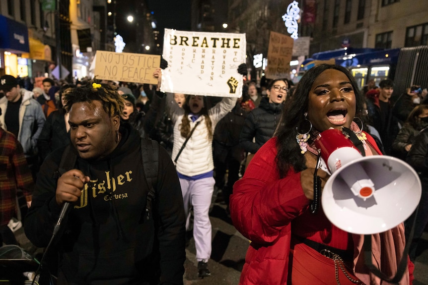 A woman walks in front of a crowd yelling into a loud speaker.