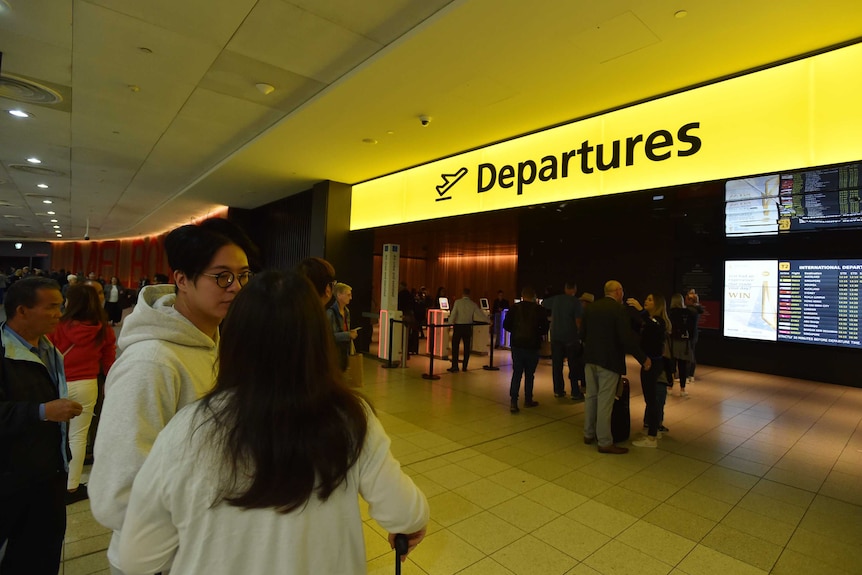 People are seen waiting in front of the yellow departures sign.