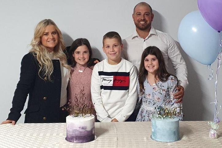 Family of five smile at camera between birthday balloons