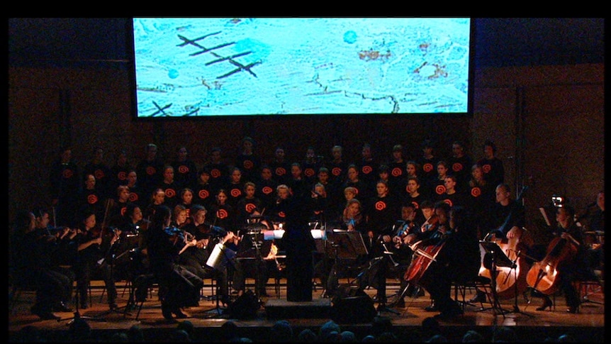 ACO and Gondwana Voices perform in semi-darkness beneath a blue projected illustration from Shaun Tan's The Red Tree.